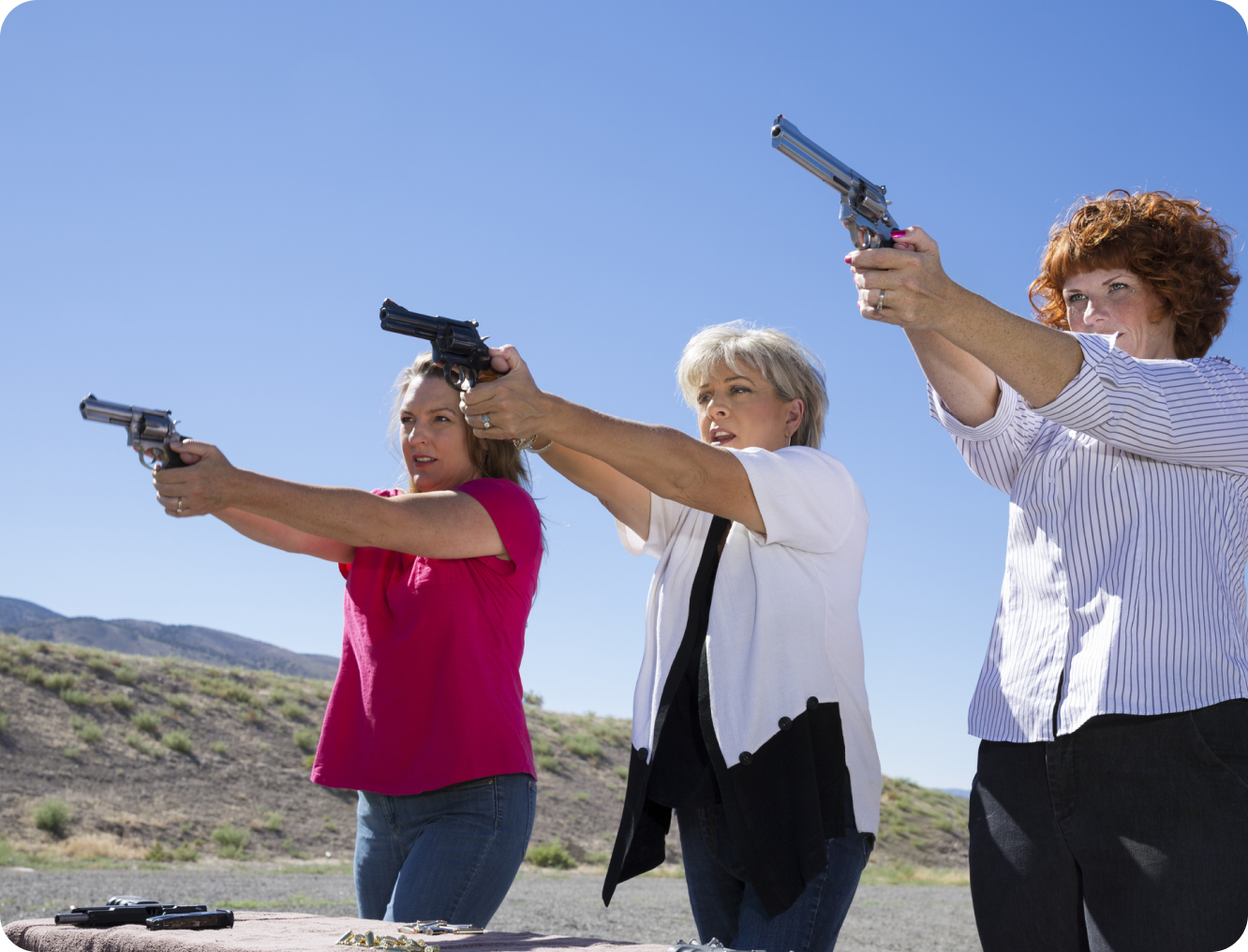 Three women aiming pistols outdoors